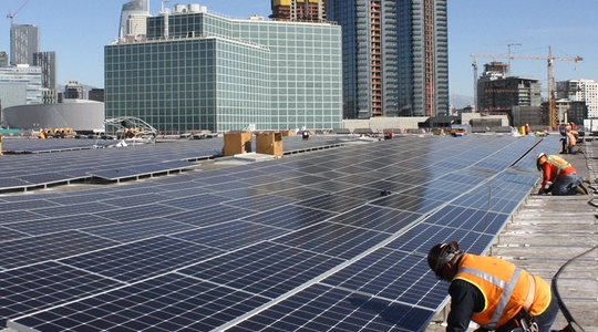 Workers install a vast array of panels atop a City building in Downtown L.A.